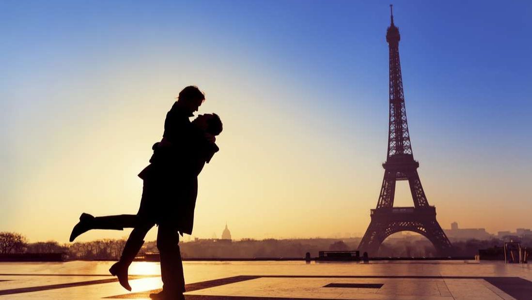 Silhouette of man romantically embracing woman in front of Eiffel Tower at dusk